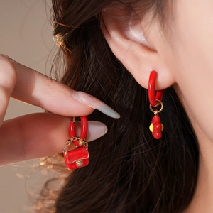 Detail of red enamel asymmetrical earrings with flower and handbag charms on a model