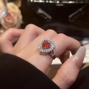 Close-up of heart-shaped red zircon ring with pearl halo and silver band on finger