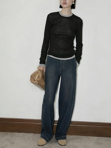 Full body shot of a model wearing a black long-sleeve knit top with wide-leg blue jeans