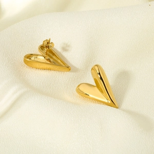 Macro view of gold heart stud earrings on silk fabric showing polished 3D metal texture
