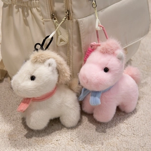 Cute plush pony keychains in white and pink hanging on a beige backpack bag