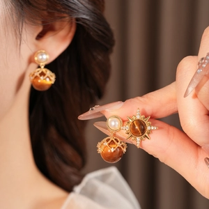 Detail of vintage gold sunburst earring with tiger eye stone and pearls on model
