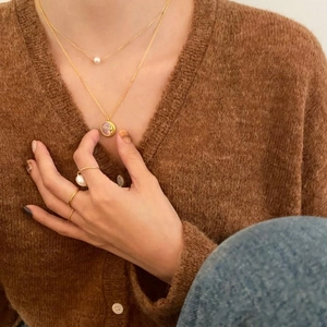 Close-up of layered gold pearl necklaces and minimalist rings worn over a brown sweater