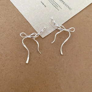 Close-up of elegant silver bow earrings with a fluid ribbon design on a neutral background