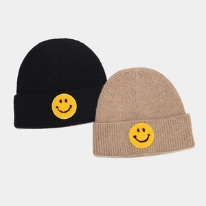 Détail de bonnets en maille côtelée noir et kaki avec écusson brodé visage souriant jaune