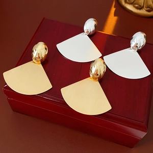 Macro detail of brushed gold and silver fan-shaped earrings on a vintage jewelry box