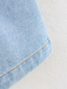 Detailed macro view of light blue denim fabric with classic orange stitching on vest