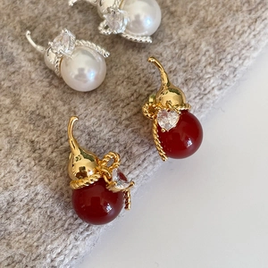Elegant gold-plated gourd stud earrings with pearls and red stones on warm knit background