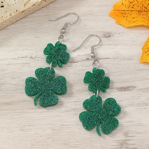 Macro view of green glitter four-leaf clover earrings on light wood texture