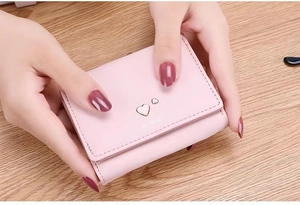 Pink PU leather tri-fold short wallet for women featuring a metal heart ornament on wood