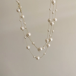 Detail of layered gold metal chains with scattered white faux pearls in a star-like design