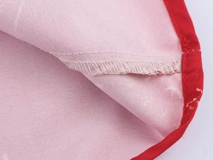 Close-up of pink fabric texture with red edge binding and detailed white overlock stitching
