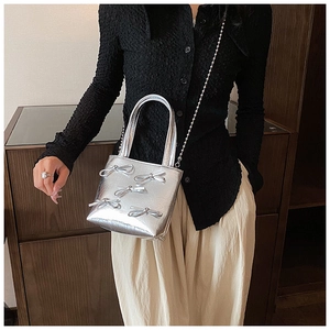 Detail of silver handbag with bow decorations and metal chain strap worn by a model