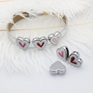 Detail view of heart-shaped charms in red and pink on silver bracelets over white feathers