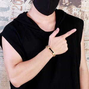 Detail of gold woven chain bracelet for men with black stripe inlay on a model's wrist