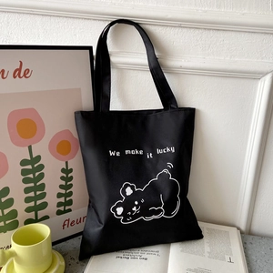 Detail of black canvas tote bag with white cartoon bear and We make it lucky text