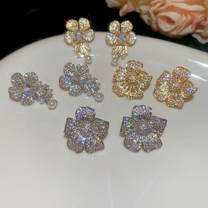 Close-up of four floral pearl and zircon earrings arranged on a white ceramic plate