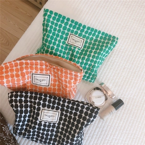 Three large capacity polka dot pouches in green, orange, and black on a bedsheet