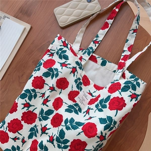 Detail shot of vintage floral canvas tote bag with red roses on a wooden surface