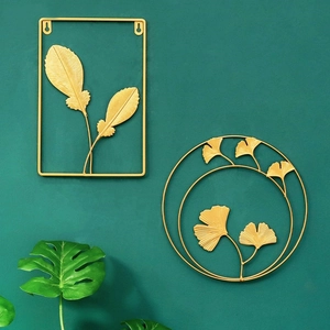 Golden iron wall art set with feather and ginkgo designs on a dark green wall