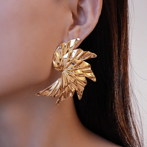 Macro shot of gold spiral leaf stud earring with polished metallic surface on model