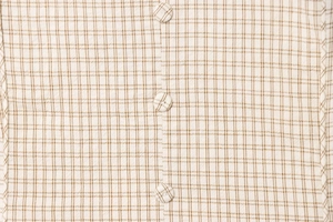 Macro shot of brown plaid fabric detail featuring covered round buttons and fine texture