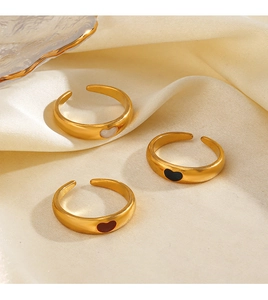 Close-up of three 18K gold plated heart rings in black, red and white on beige silk fabric