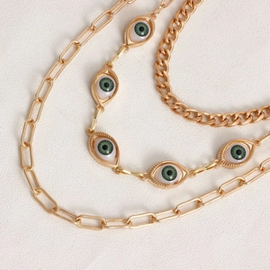Detail of multilayer gold waist chain with green eye charms on white textured surface
