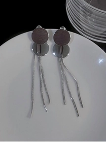 Macro detail of silver tassel earrings with brushed metal studs on white ceramic plate