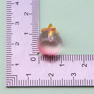 Detailed view of a mini peach fruit charm with golden ring loop on a measuring scale