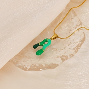 Gros plan du pendentif lettre R en émail vert sur une chaîne en acier inoxydable doré