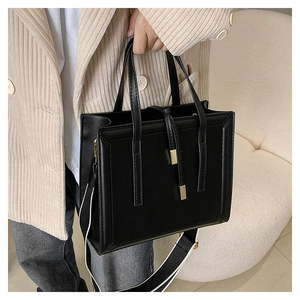 Close-up of black leather tote bag with wide contrast shoulder strap and zipper