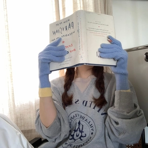 Detail of blue knitted gloves with yellow cuffs being used by a person reading a book