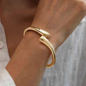 Macro detail of golden irregular waterdrop cuff bracelet showing polished metal texture