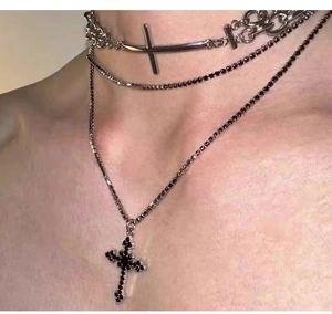 Detail of layered silver snake chain necklaces with black gemstone cross pendant
