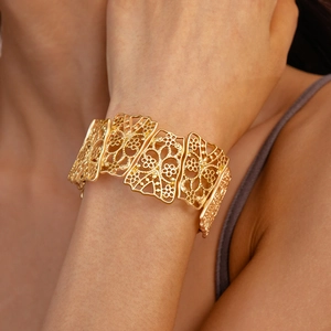 Detailed view of wide gold matte hollow floral bangle worn on a model's wrist