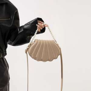 Detailed shot of beige shell-shaped bag with pearl handle and vertical stripes