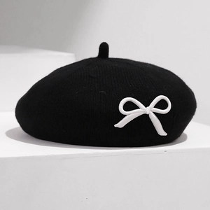 Détail du béret en tricot noir montrant la broderie de nœud blanc et la texture douce