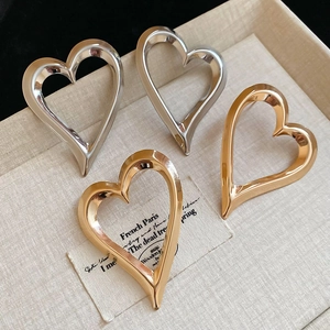 Macro view of gold and silver hollow heart-shaped stud earrings on a textured beige tray