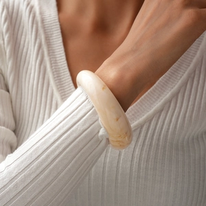 Gros plan d'un bracelet jonc épais en résine crème avec texture marbrée ambre