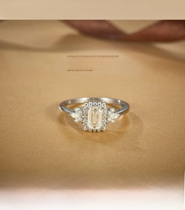Detail of emerald cut moissanite ring with marquise side stones on gold satin fabric