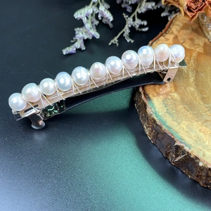 Close-up of white pearls with silver wire on a bohemian spring hair clip over wood