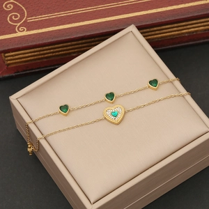 Elegant emerald heart pendant set with dual layered gold chains on jewelry box