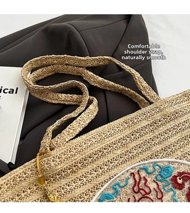 Close-up of woven straw shoulder bag featuring ethnic embroidery and golden tassel detail