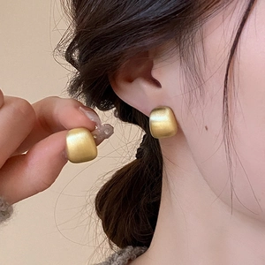 Detailed close-up of matte gold geometric square stud earrings on a model's ear