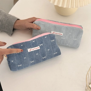 Close-up of denim pencil cases with bow embroidery and contrasting pink zippers