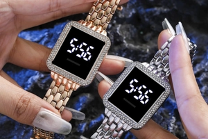 Detail view of square diamond LED watches in rose gold and silver on a dark rock background