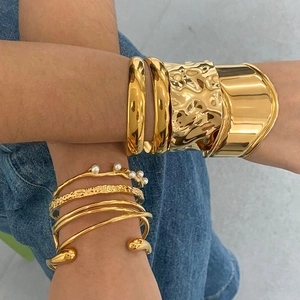 Stacked gold stainless steel bracelets with hammered texture and pearl details on denim