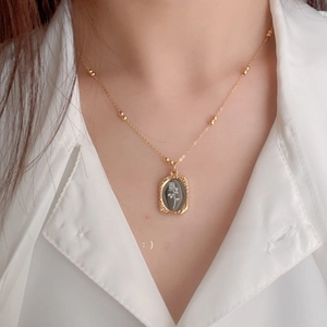 Macro view of gold rose relief pendant on a beaded chain over a white shirt