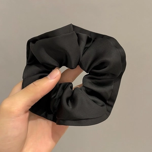 Detailed close-up of large black satin scrunchie with layered ruffle texture and subtle gloss